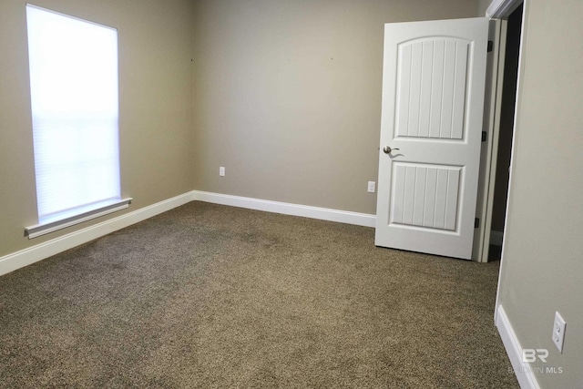 unfurnished room featuring baseboards and dark carpet