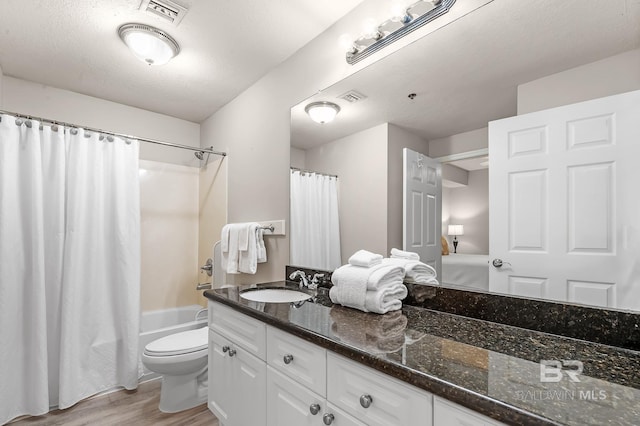 full bathroom with visible vents, toilet, wood finished floors, shower / bath combo with shower curtain, and vanity