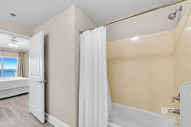 ensuite bathroom with baseboards, ceiling fan, ensuite bath, wood finished floors, and shower / bath combo with shower curtain