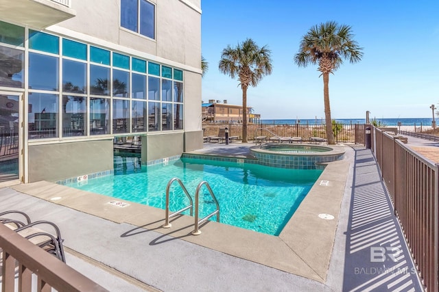 community pool featuring a patio, a water view, fence, and a hot tub