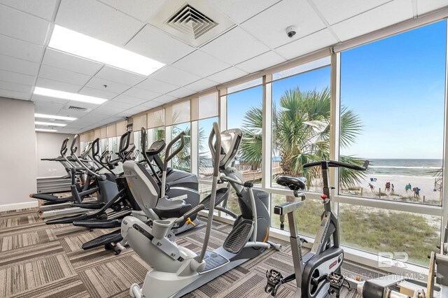 exercise room with carpet floors, a view of the beach, visible vents, and a water view