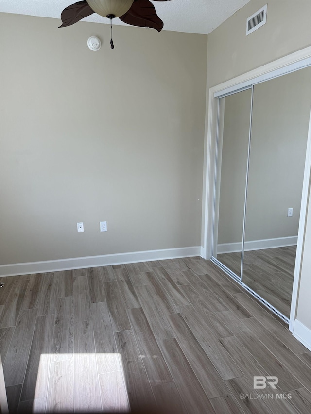 unfurnished bedroom featuring baseboards, a closet, wood finished floors, and visible vents
