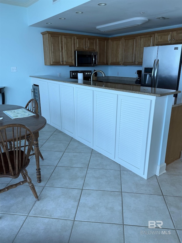 kitchen with dark stone counters, stainless steel appliances, visible vents, and light tile patterned floors
