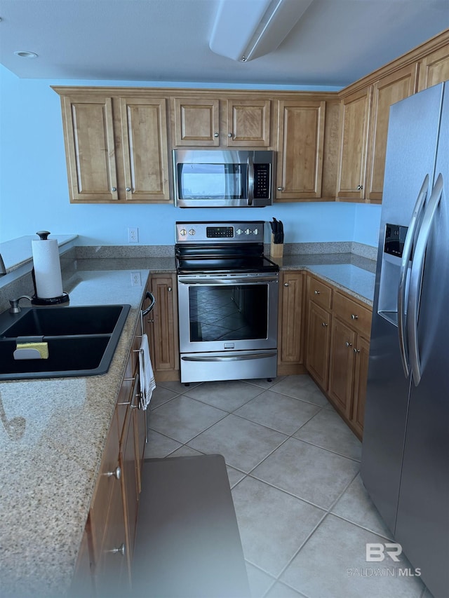 kitchen featuring brown cabinetry, a sink, light tile patterned floors, and stainless steel appliances