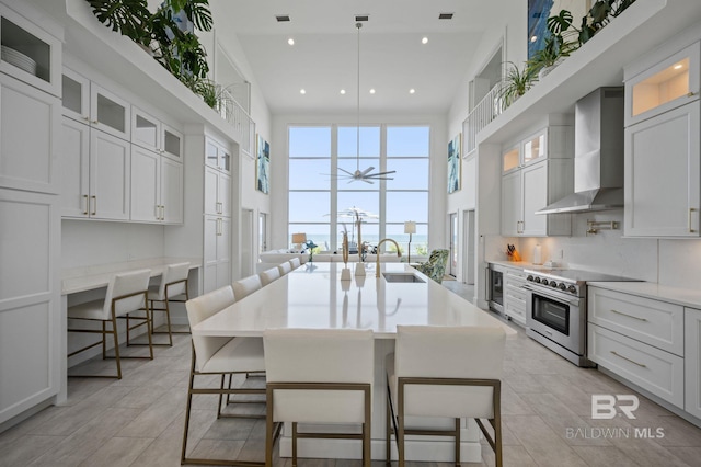 kitchen with a breakfast bar, stainless steel stove, a center island with sink, and wall chimney range hood