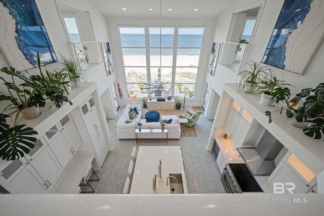 living area featuring a beach view, a high ceiling, a water view, and recessed lighting