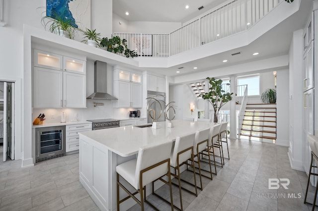 kitchen featuring an island with sink, appliances with stainless steel finishes, glass insert cabinets, wall chimney range hood, and white cabinetry