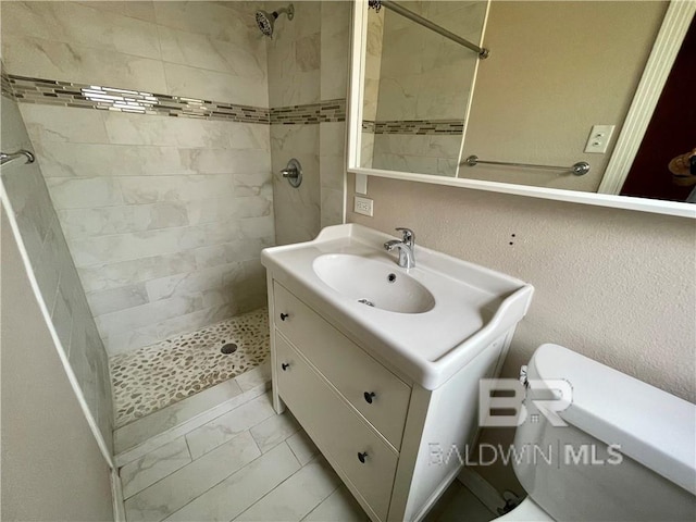 bathroom featuring toilet, vanity, and a tile shower