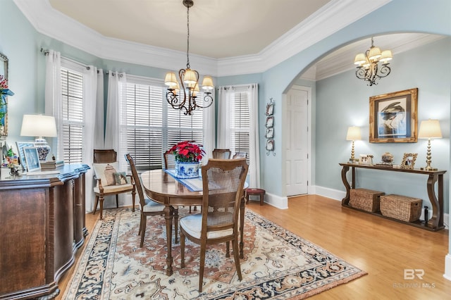 dining space with crown molding, arched walkways, a chandelier, and light wood-style floors