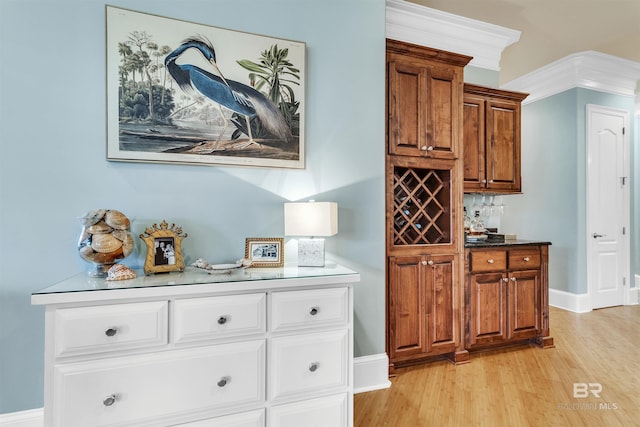 bar featuring baseboards, crown molding, and light wood finished floors