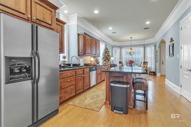 kitchen with light wood-style floors, appliances with stainless steel finishes, a kitchen island, a kitchen bar, and a sink