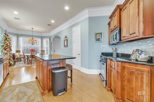 kitchen featuring light wood finished floors, stainless steel appliances, a notable chandelier, brown cabinetry, and arched walkways
