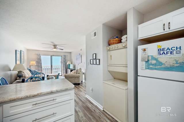 kitchen featuring white refrigerator, stacked washing maching and dryer, a textured ceiling, and white cabinets