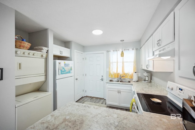 kitchen featuring sink, white appliances, stacked washer and clothes dryer, white cabinets, and decorative light fixtures