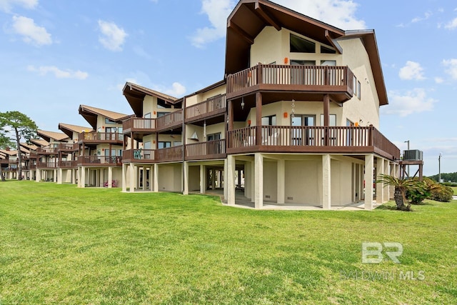 rear view of house featuring stucco siding, a lawn, a balcony, and central AC unit