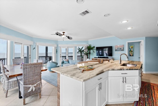 kitchen featuring a sink, open floor plan, crown molding, a kitchen island with sink, and light stone countertops