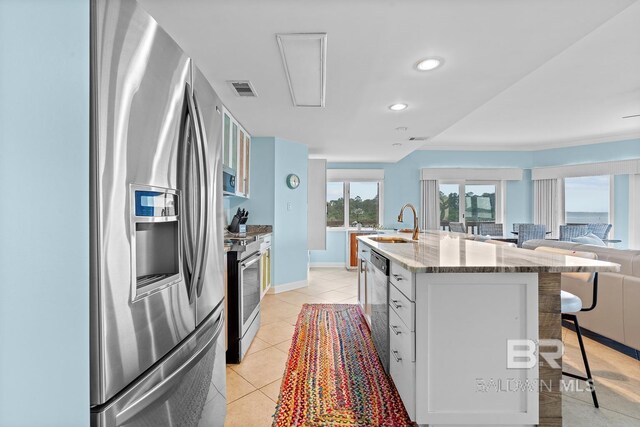kitchen with stainless steel appliances, a breakfast bar area, a sink, light stone counters, and a kitchen island with sink