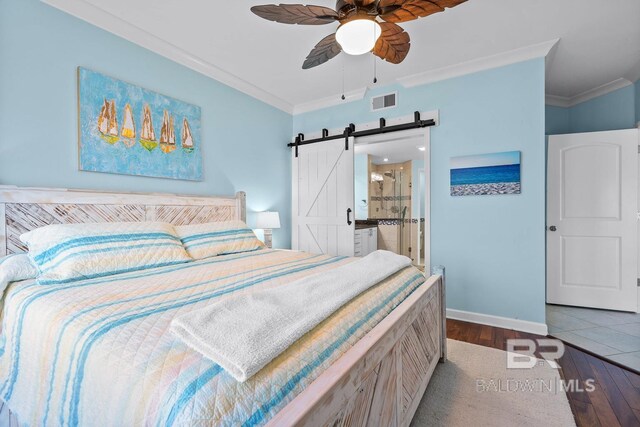 bedroom featuring a barn door, crown molding, hardwood / wood-style floors, baseboards, and connected bathroom