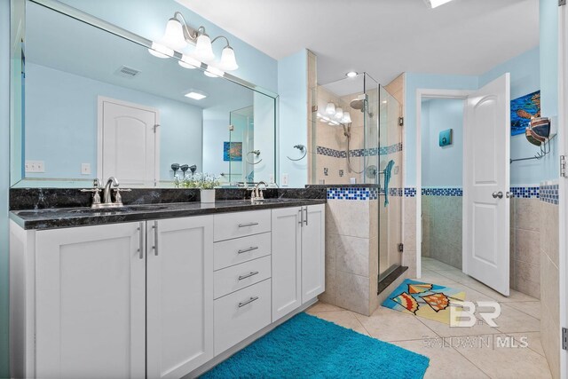 bathroom featuring tile walls, tile patterned flooring, a shower stall, double vanity, and a wainscoted wall