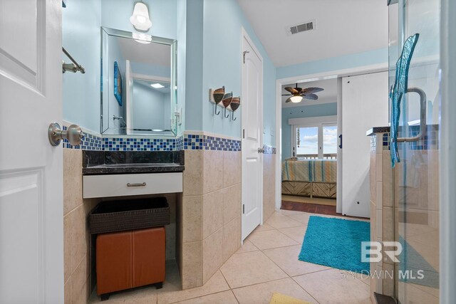 bathroom with tile walls, ensuite bathroom, tile patterned flooring, ceiling fan, and vanity