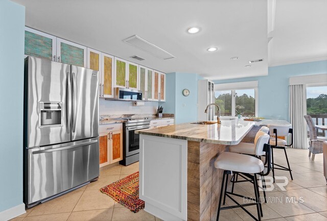 kitchen with appliances with stainless steel finishes, a sink, a breakfast bar area, glass insert cabinets, and recessed lighting