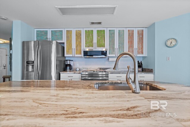 kitchen with stainless steel appliances, a sink, light stone countertops, glass insert cabinets, and white cabinetry