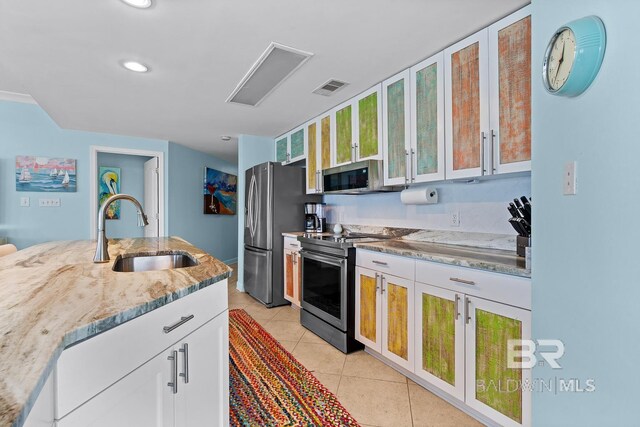 kitchen featuring a sink, appliances with stainless steel finishes, light stone countertops, glass insert cabinets, and light tile patterned flooring