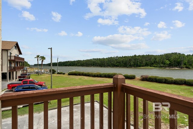 view of green lawn featuring a water view, a balcony, and a wooded view