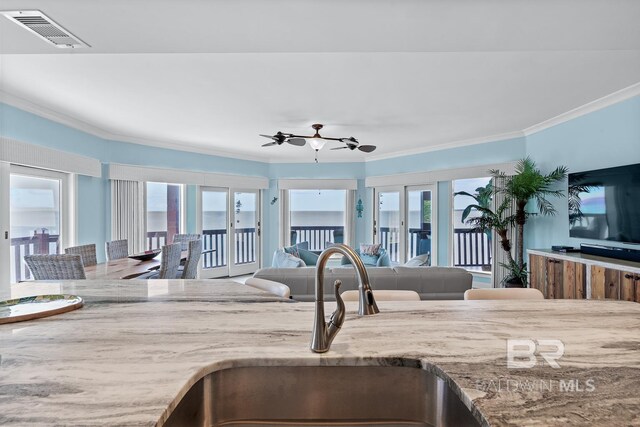 kitchen with a sink, ornamental molding, open floor plan, light stone countertops, and plenty of natural light