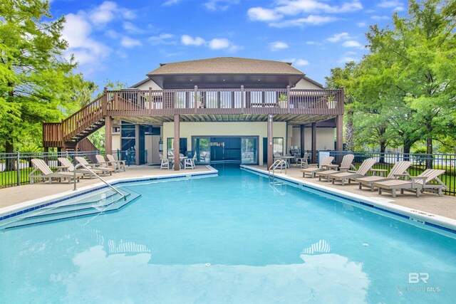 community pool featuring fence, a patio, stairway, and a wooden deck