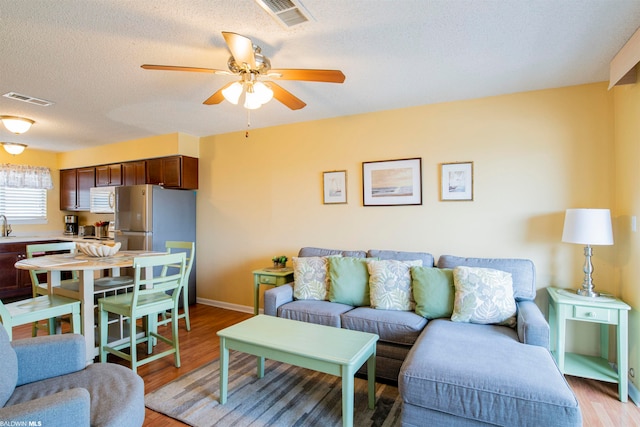 living room with ceiling fan, light hardwood / wood-style floors, and a textured ceiling