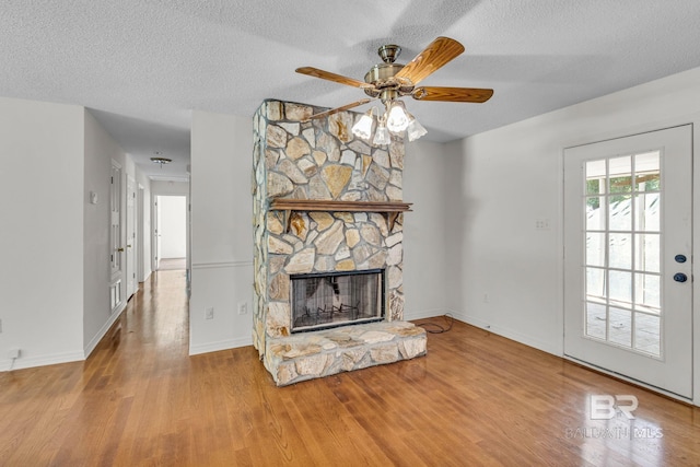 unfurnished living room featuring wood-type flooring, ceiling fan, a textured ceiling, and a stone fireplace