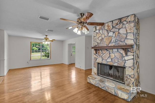 living room with ceiling fan, a textured ceiling, a fireplace, and light wood-type flooring