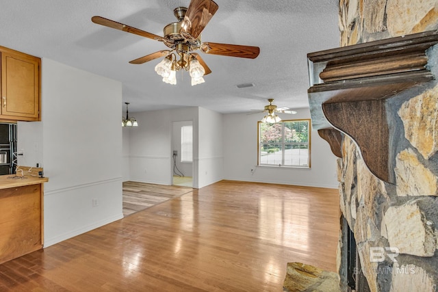 unfurnished living room featuring a textured ceiling, ceiling fan with notable chandelier, and light hardwood / wood-style flooring