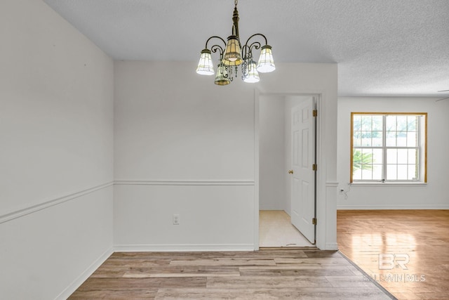 unfurnished room featuring a notable chandelier, light wood-type flooring, and a textured ceiling