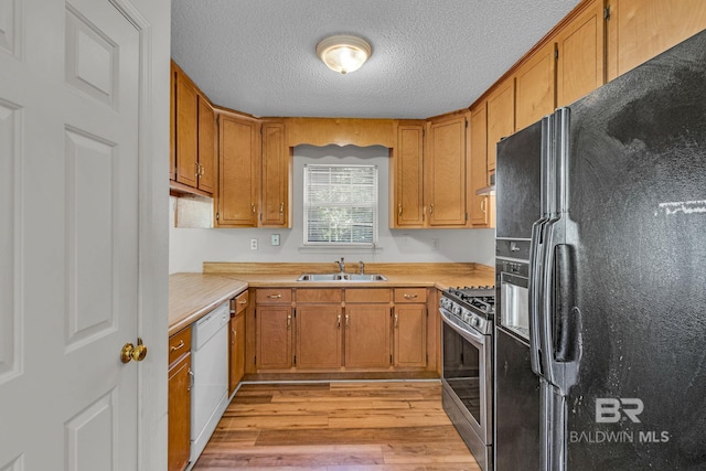 kitchen featuring black fridge, sink, stainless steel gas range oven, light hardwood / wood-style flooring, and white dishwasher