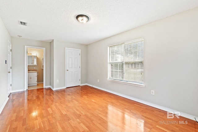 unfurnished bedroom with a textured ceiling, ensuite bath, and light hardwood / wood-style flooring