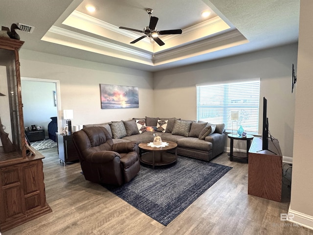 living room with ornamental molding, a tray ceiling, and wood finished floors