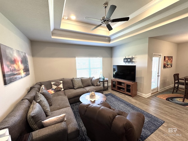 living room featuring a tray ceiling, crown molding, a ceiling fan, wood finished floors, and baseboards