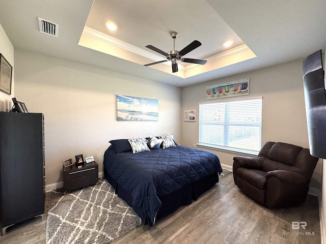 bedroom featuring ornamental molding, a tray ceiling, visible vents, and wood finished floors