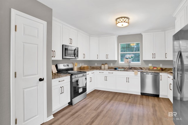 kitchen featuring appliances with stainless steel finishes, light hardwood / wood-style floors, white cabinetry, and stone counters