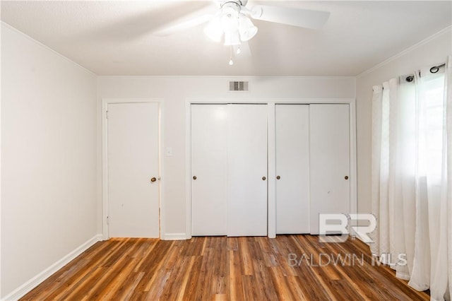 unfurnished bedroom featuring dark hardwood / wood-style floors, crown molding, ceiling fan, and multiple closets