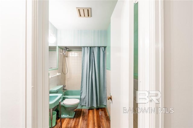 bathroom with shower / tub combo with curtain, hardwood / wood-style floors, and toilet