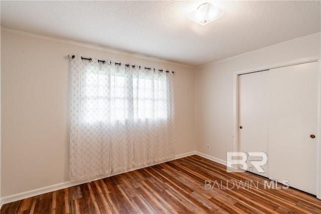 empty room featuring dark wood-type flooring, a textured ceiling, and ornamental molding