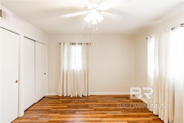 unfurnished bedroom featuring ceiling fan, wood-type flooring, crown molding, and a closet