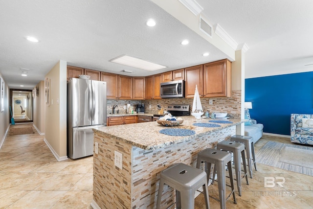 kitchen featuring stainless steel appliances, a breakfast bar, decorative backsplash, and light stone countertops