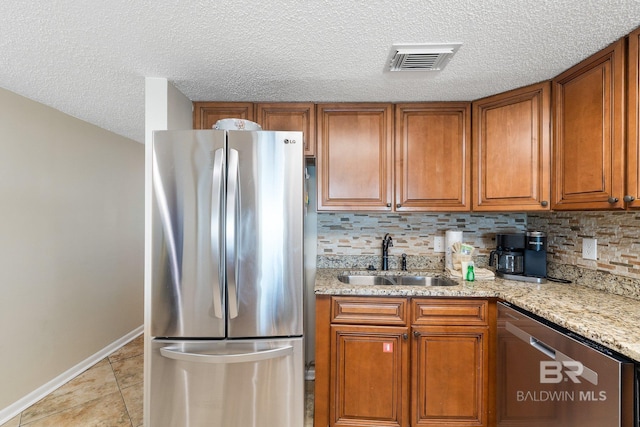 kitchen featuring light stone countertops, a sink, visible vents, appliances with stainless steel finishes, and brown cabinets