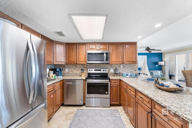 kitchen with stainless steel appliances, brown cabinets, backsplash, and light stone countertops