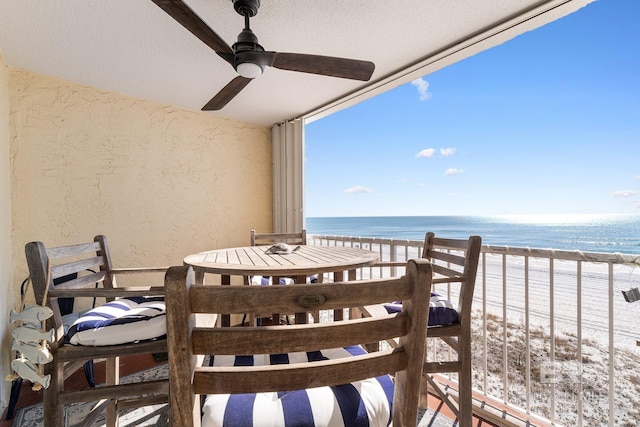 balcony with a water view, a beach view, and a ceiling fan