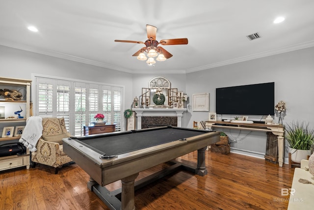 recreation room featuring visible vents, ornamental molding, wood finished floors, a fireplace, and a ceiling fan